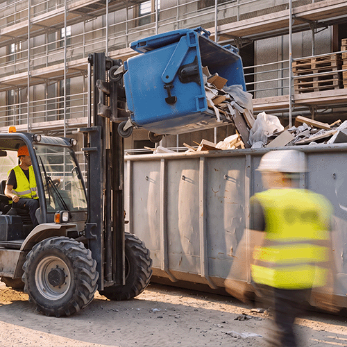 Entsorgungslogistik – Stapler entleert Bauschuttcontainer in eine Mulde auf der Baustelle