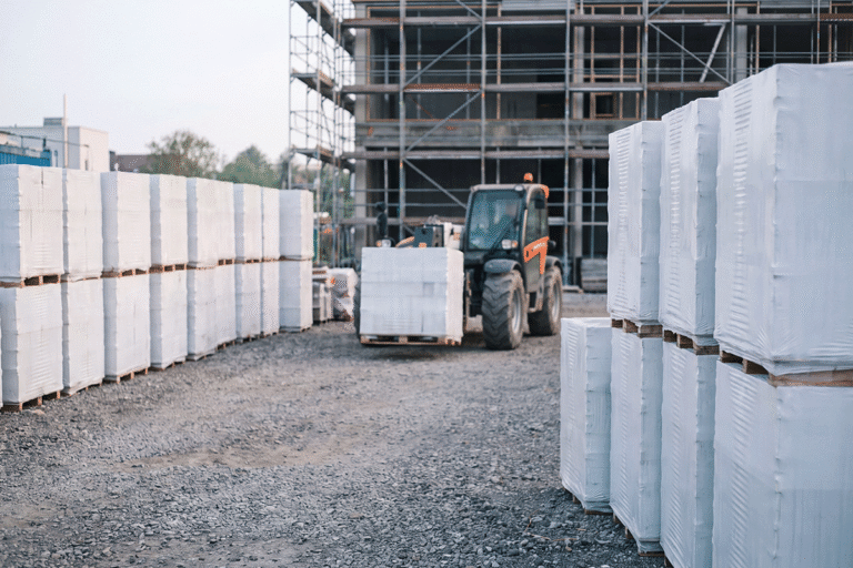Materiallager mit palettiertem Baumaterial und Teleskoplader auf der Baustelle