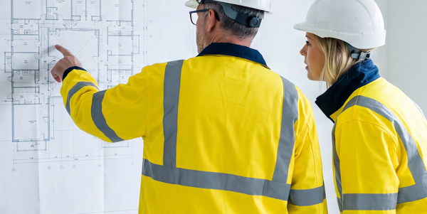 Zwei UTS Baulogistik Mitarbeiter mit Helm und Warnjacke besprechen einen Bauplan