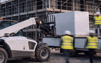Lieferlogistik auf der Baustelle – Teleskoplader entlädt Baumaterial vor dem Gerüst
